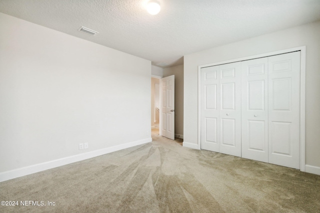 unfurnished bedroom with light colored carpet, a textured ceiling, and a closet