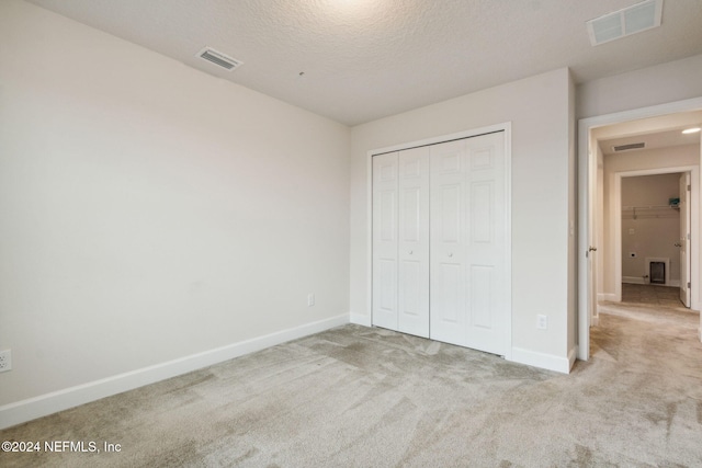 unfurnished bedroom with a textured ceiling, light carpet, and a closet