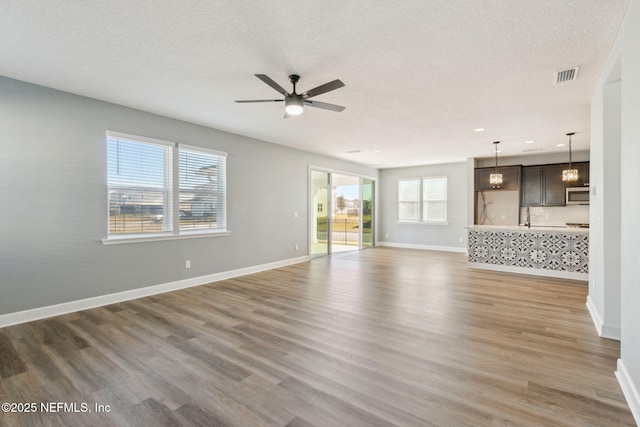 unfurnished living room featuring a textured ceiling, dark hardwood / wood-style flooring, and ceiling fan with notable chandelier