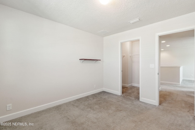 unfurnished bedroom featuring a textured ceiling, a walk in closet, light colored carpet, and a closet