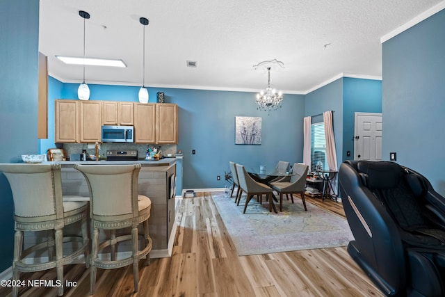 kitchen with light brown cabinets, ornamental molding, pendant lighting, an inviting chandelier, and light hardwood / wood-style floors