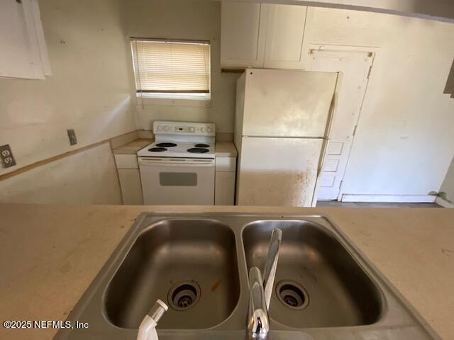 kitchen featuring white cabinets, white appliances, light countertops, and a sink