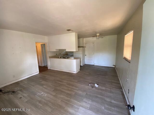 unfurnished living room with visible vents, baseboards, a ceiling fan, and dark wood-style flooring