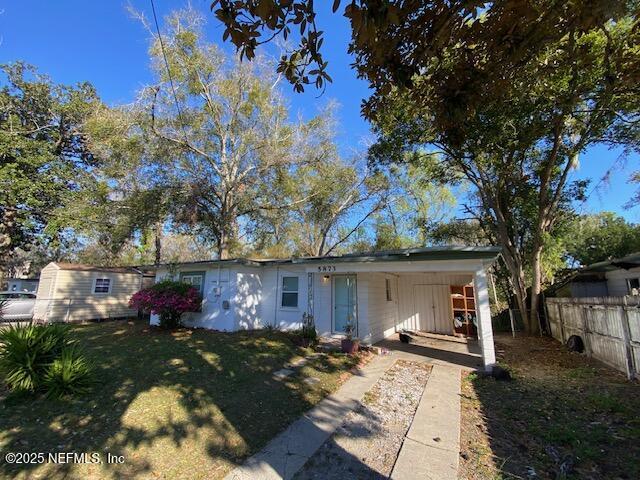 view of front facade with a carport, concrete driveway, a front lawn, and fence