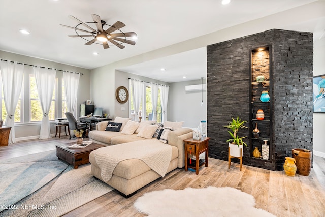 living room featuring a wall mounted AC, light wood-type flooring, and ceiling fan