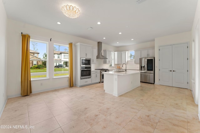 kitchen with a center island with sink, white cabinets, wall chimney range hood, and appliances with stainless steel finishes