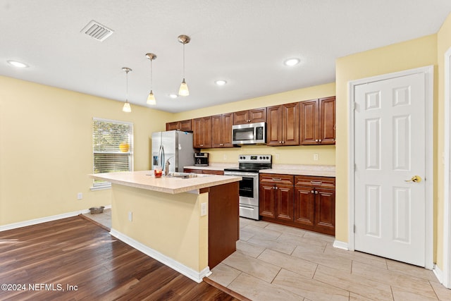 kitchen with hanging light fixtures, a center island with sink, light hardwood / wood-style flooring, sink, and stainless steel appliances