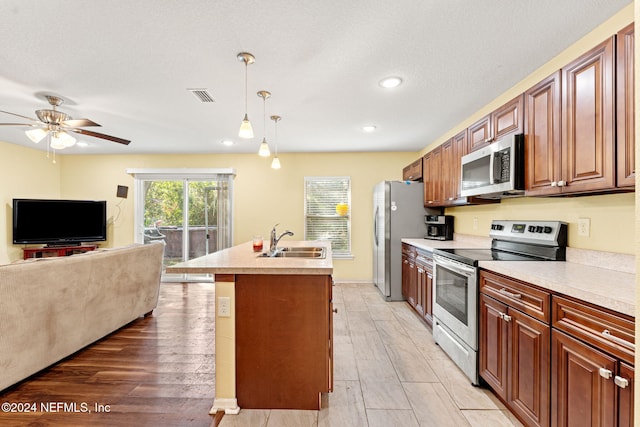 kitchen with appliances with stainless steel finishes, a kitchen island with sink, pendant lighting, light hardwood / wood-style floors, and sink