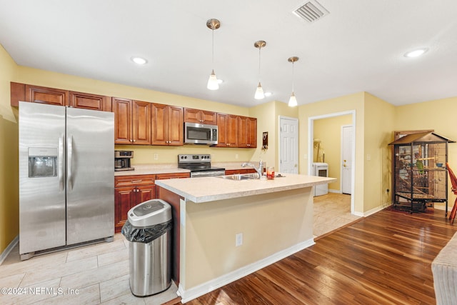 kitchen featuring appliances with stainless steel finishes, a kitchen island with sink, pendant lighting, light hardwood / wood-style floors, and sink