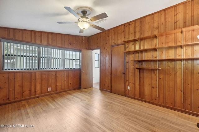 empty room with light wood-type flooring, wood walls, and ceiling fan