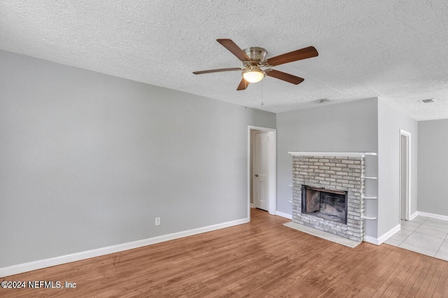 unfurnished living room featuring a fireplace, ceiling fan, a textured ceiling, and light hardwood / wood-style flooring