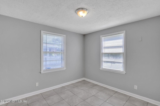 unfurnished room featuring plenty of natural light, a textured ceiling, and light tile patterned floors