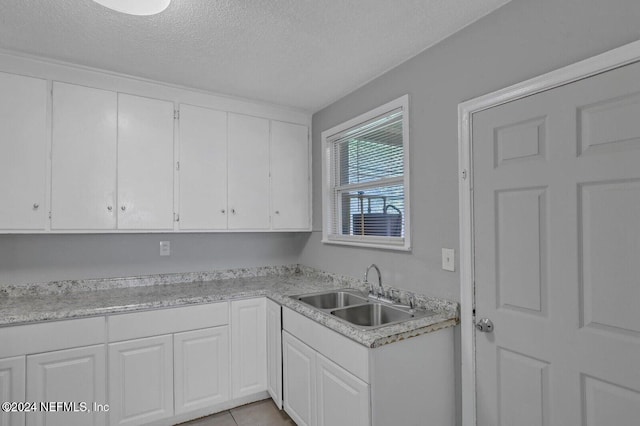 kitchen featuring white cabinetry, sink, light tile patterned floors, and a textured ceiling