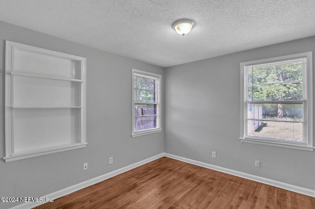 empty room with hardwood / wood-style floors, a healthy amount of sunlight, a textured ceiling, and built in shelves