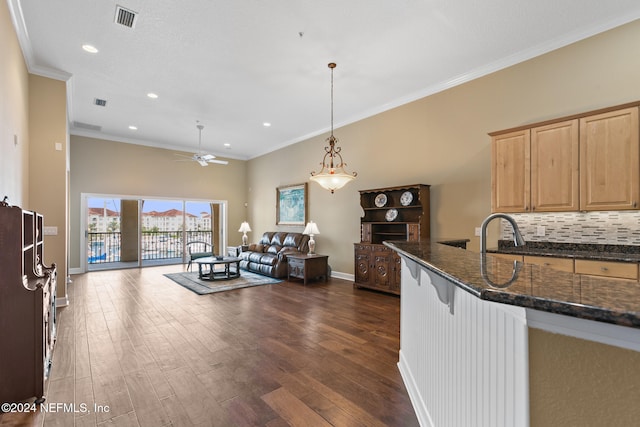 kitchen featuring tasteful backsplash, dark wood-type flooring, ornamental molding, hanging light fixtures, and dark stone countertops