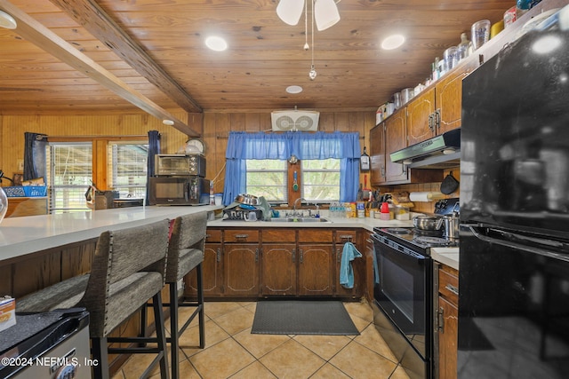 kitchen with wood walls, black appliances, light tile patterned floors, sink, and wooden ceiling