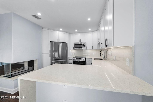 kitchen with kitchen peninsula, stainless steel appliances, white cabinets, and sink