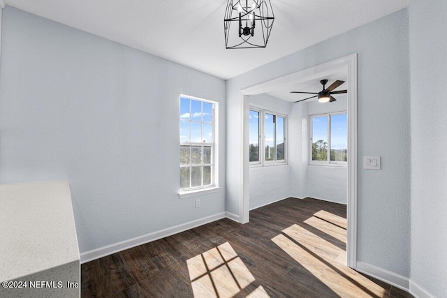 empty room featuring ceiling fan with notable chandelier and dark wood-type flooring