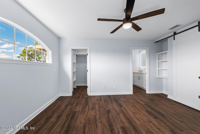 unfurnished bedroom with dark hardwood / wood-style flooring, a barn door, ensuite bathroom, and a spacious closet