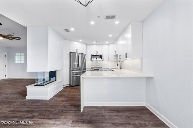 kitchen with kitchen peninsula, appliances with stainless steel finishes, dark hardwood / wood-style flooring, sink, and white cabinetry