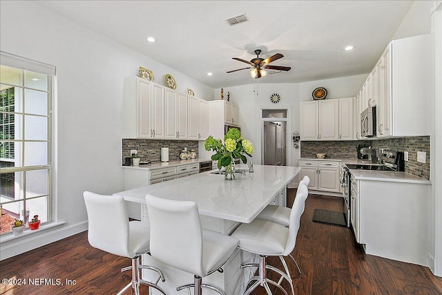 kitchen with white cabinetry, appliances with stainless steel finishes, a center island with sink, and dark hardwood / wood-style flooring