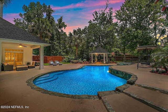 pool at dusk with a patio area and a gazebo