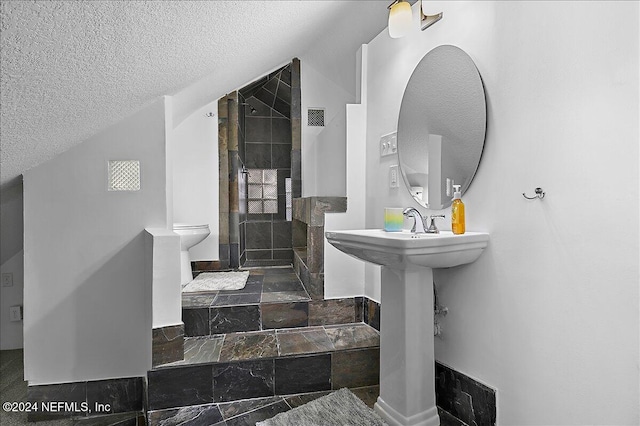 bathroom with toilet, a textured ceiling, and a tile shower