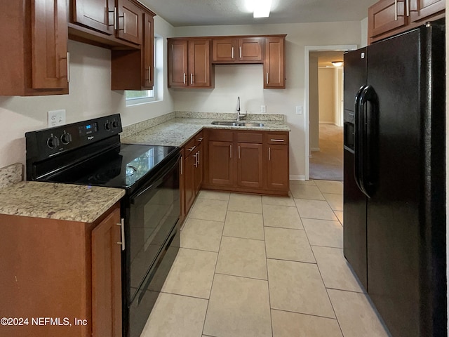 kitchen featuring light stone countertops, black appliances, sink, and light tile patterned flooring