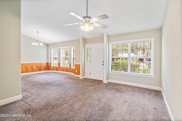 spare room with carpet floors, ceiling fan with notable chandelier, wood walls, and lofted ceiling