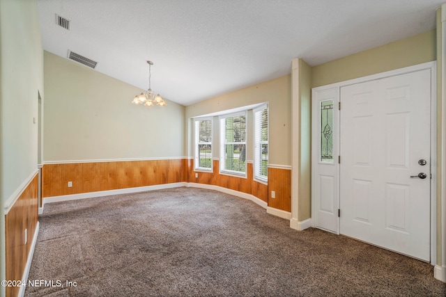 carpeted entrance foyer with wooden walls, a textured ceiling, lofted ceiling, and a notable chandelier