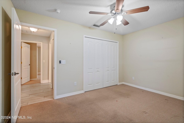 unfurnished bedroom with a textured ceiling, light carpet, ceiling fan, and a closet