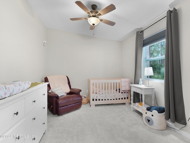 carpeted bedroom featuring a crib and ceiling fan