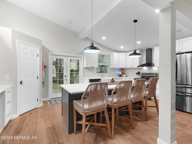 kitchen with appliances with stainless steel finishes, light hardwood / wood-style flooring, a kitchen island, white cabinets, and wall chimney range hood