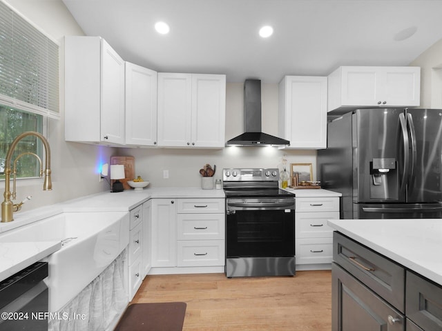 kitchen featuring appliances with stainless steel finishes, sink, white cabinets, wall chimney exhaust hood, and light hardwood / wood-style flooring