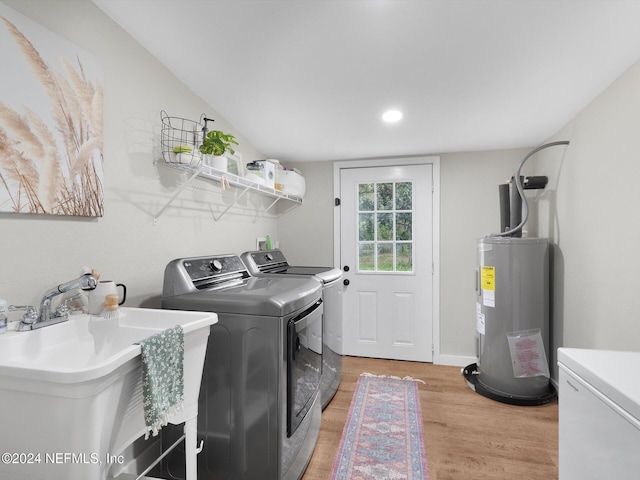 washroom featuring water heater, sink, washer and dryer, and light hardwood / wood-style flooring