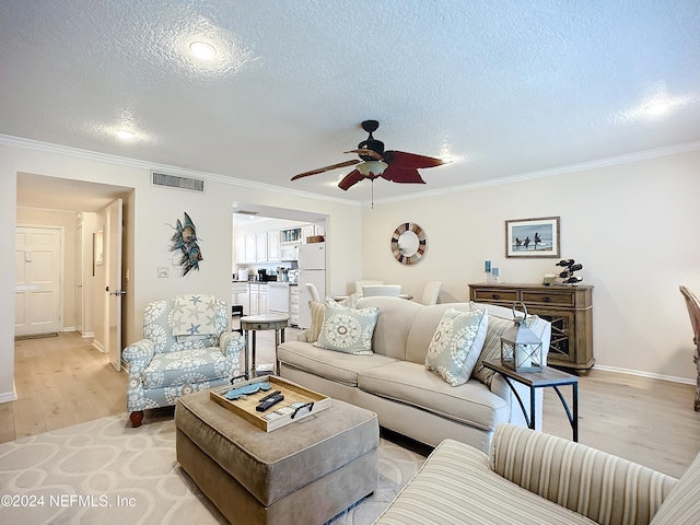 living room featuring light wood-type flooring, a textured ceiling, ceiling fan, and ornamental molding