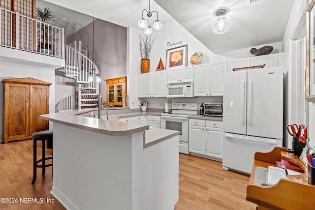 kitchen with a kitchen bar, kitchen peninsula, white appliances, pendant lighting, and white cabinets