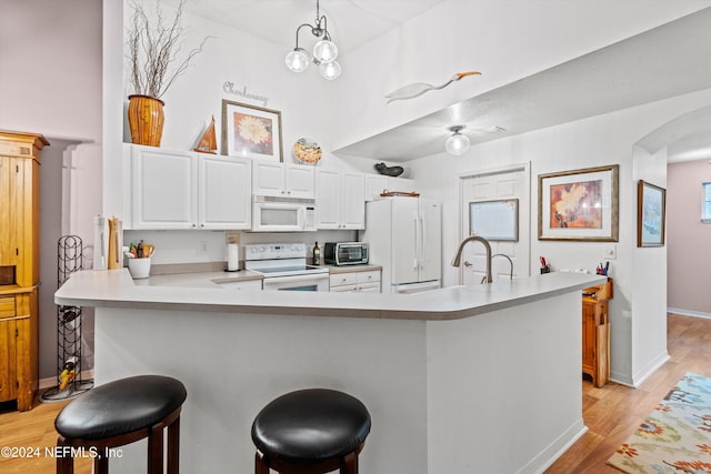 kitchen with kitchen peninsula, white appliances, decorative light fixtures, light hardwood / wood-style flooring, and white cabinets