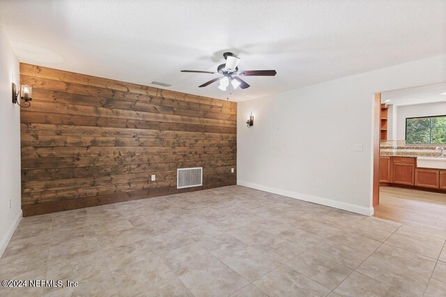 empty room with wood walls, ceiling fan, and sink