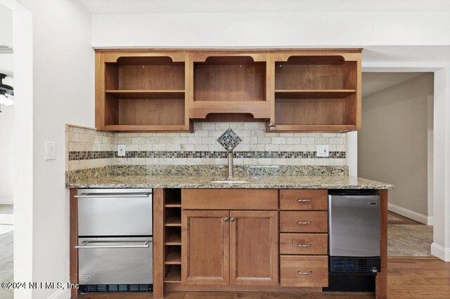 kitchen with hardwood / wood-style flooring, stainless steel refrigerator, sink, light stone counters, and tasteful backsplash