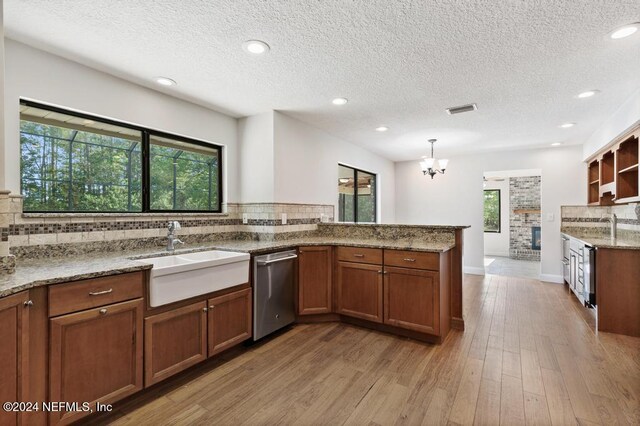 kitchen with light hardwood / wood-style floors, kitchen peninsula, hanging light fixtures, sink, and stainless steel dishwasher