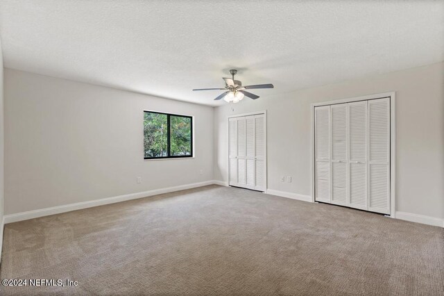 unfurnished bedroom featuring ceiling fan, a textured ceiling, multiple closets, and carpet