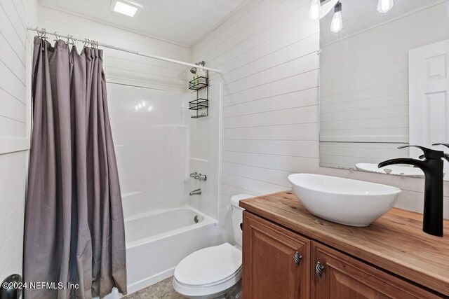 full bathroom featuring wood walls, shower / bath combo with shower curtain, vanity, and toilet