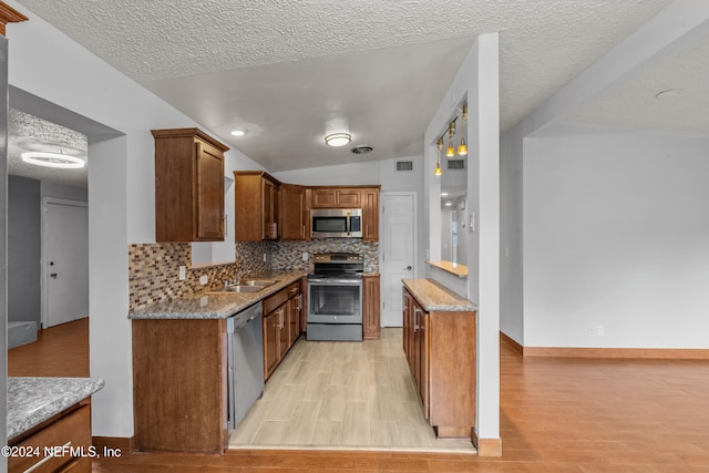 kitchen featuring a textured ceiling, light wood-type flooring, lofted ceiling, and appliances with stainless steel finishes