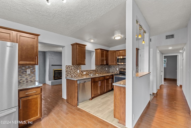 kitchen with light stone countertops, stainless steel appliances, backsplash, lofted ceiling, and light wood-type flooring