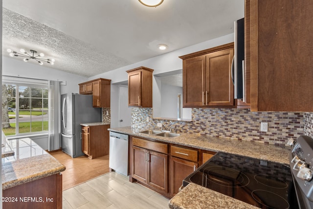 kitchen featuring appliances with stainless steel finishes, light wood-type flooring, tasteful backsplash, a textured ceiling, and sink