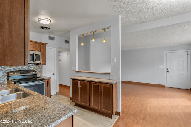 kitchen featuring sink, decorative backsplash, a textured ceiling, appliances with stainless steel finishes, and light hardwood / wood-style floors