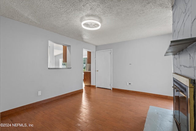 unfurnished living room featuring a textured ceiling, light hardwood / wood-style flooring, and a tiled fireplace