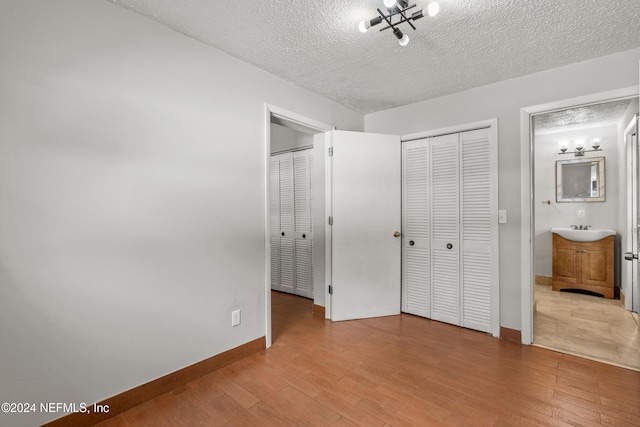 unfurnished bedroom with ensuite bathroom, a textured ceiling, and light wood-type flooring