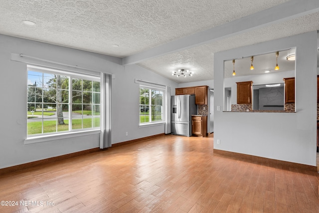 unfurnished living room with vaulted ceiling with beams, light hardwood / wood-style floors, and a textured ceiling